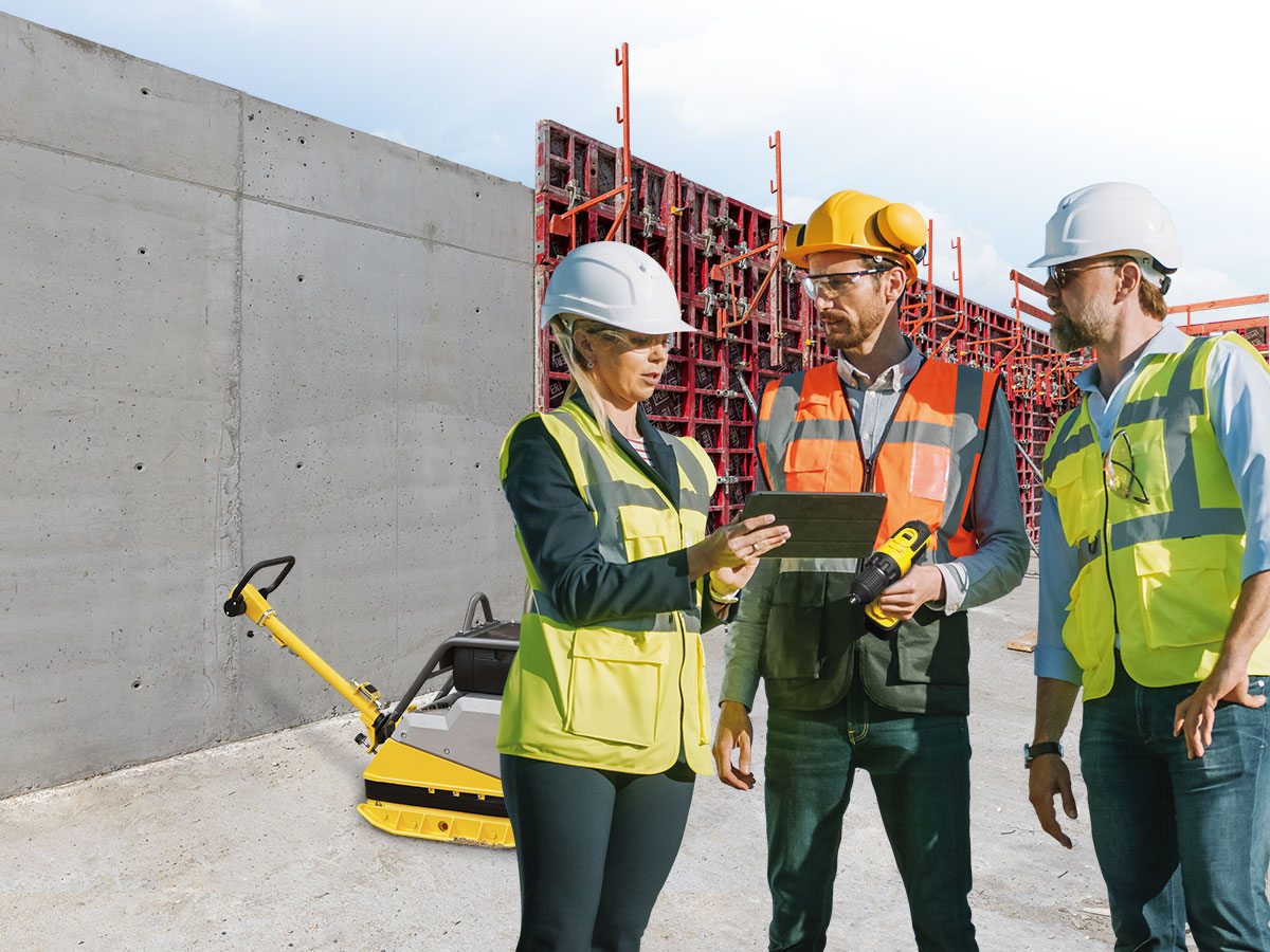 Drei Bauarbeiter mit Tablet und Akkuschrauber auf einer Baustelle.