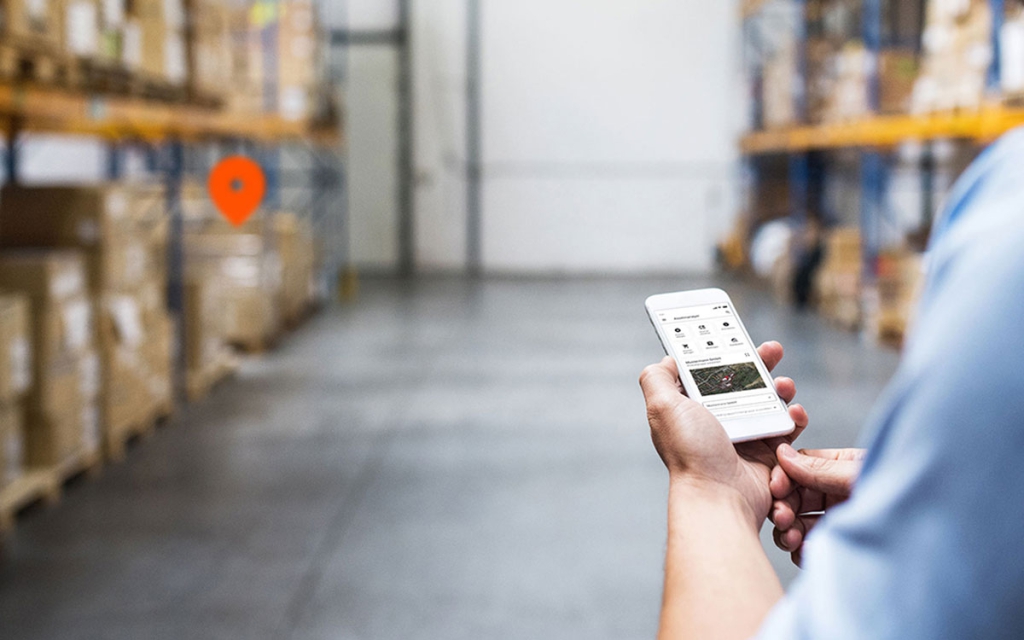 Lagerhalle mit verschiedenen Assets und Smartphone mit der App Assetmanager.